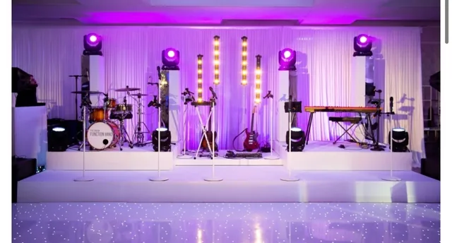 Stage on white risers with purple moving lights, marquee light columns and an LED dance floor