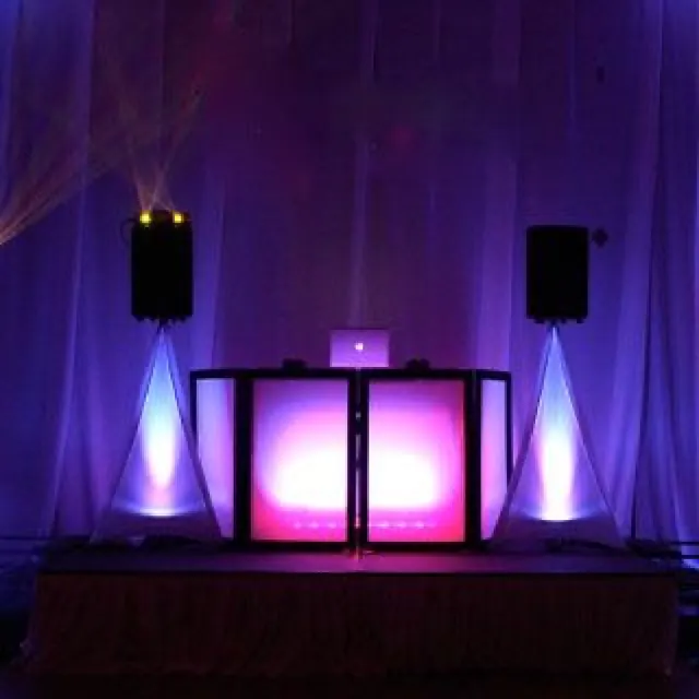 DJ booth lit in violet and pink with uplit drapes